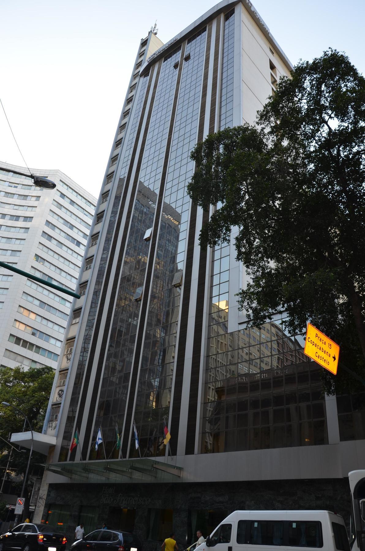 Hotel Atlantico Tower Rio de Janeiro Exterior photo The photo shows a city street with tall buildings. In the foreground, there is a modern glass skyscraper featuring reflective surfaces and vertical lines. Next to it, there's another building with a different architectural style, also made of glass. 
